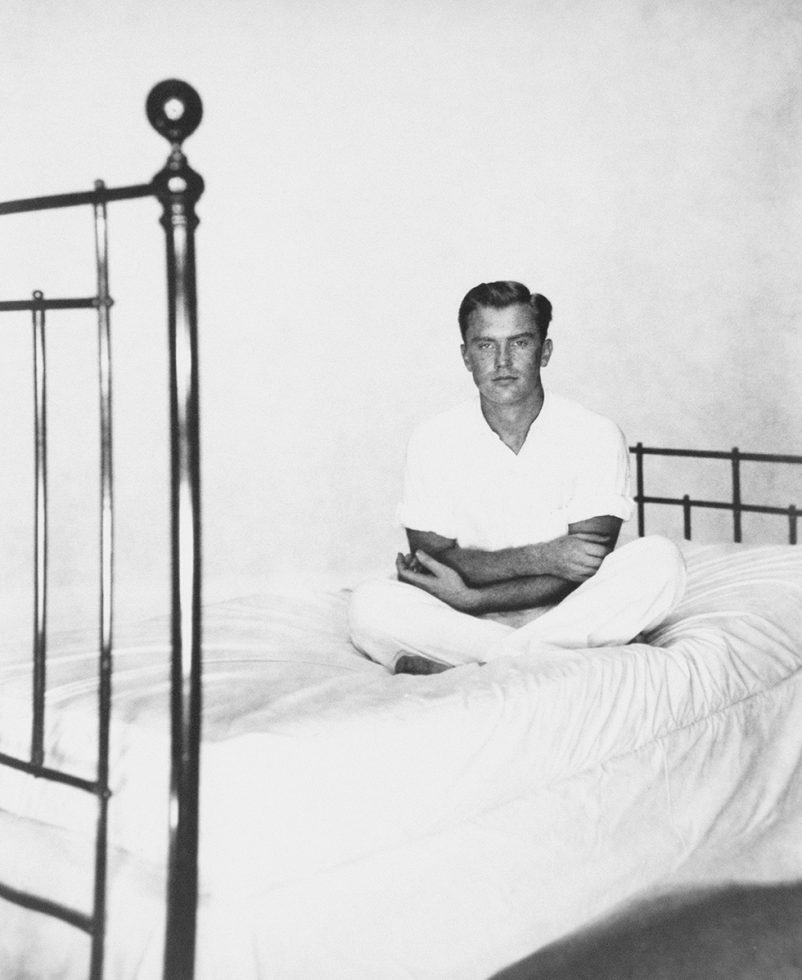 Alexander Jensen Yow wearing white sitting on a bed with white sheets