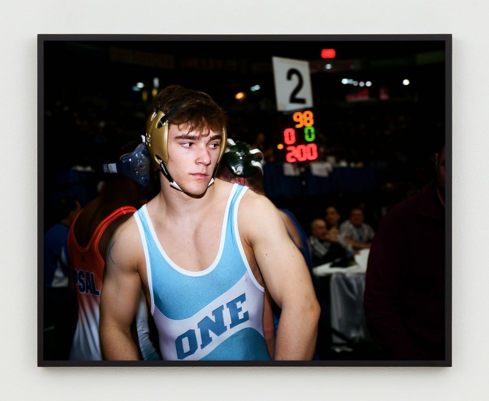 This is a photograph of a wrestler with gold head gear and a light blue singlet.