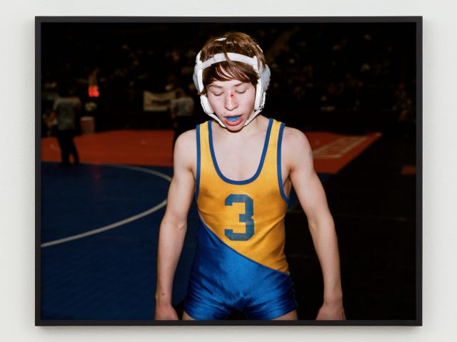 This is a photograph of a young wrestler in his gear and a blue mouth guard.