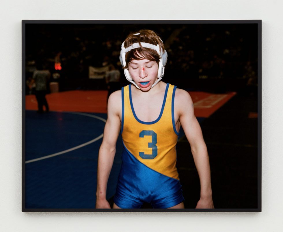 This is a photograph of a young wrestler in his gear and a blue mouth guard.