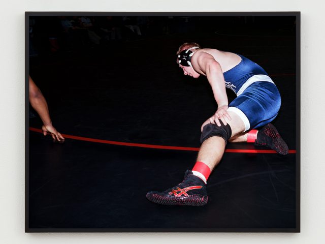 This is a photograph of a wrestler sitting on the mat with one leg out to the side.