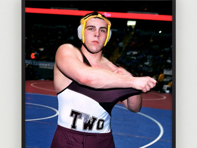 This is a photographic portrait of a wrestler adjusting his uniform.