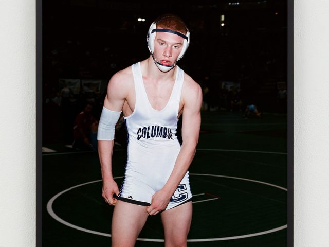 This is a color photograph of a panting, red-headed wrestler in a white Columbia singlet and headgear.