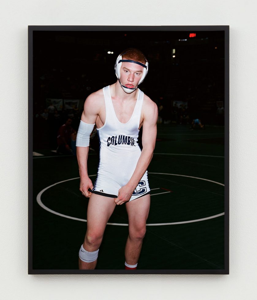 This is a color photograph of a panting, red-headed wrestler in a white Columbia singlet and headgear.