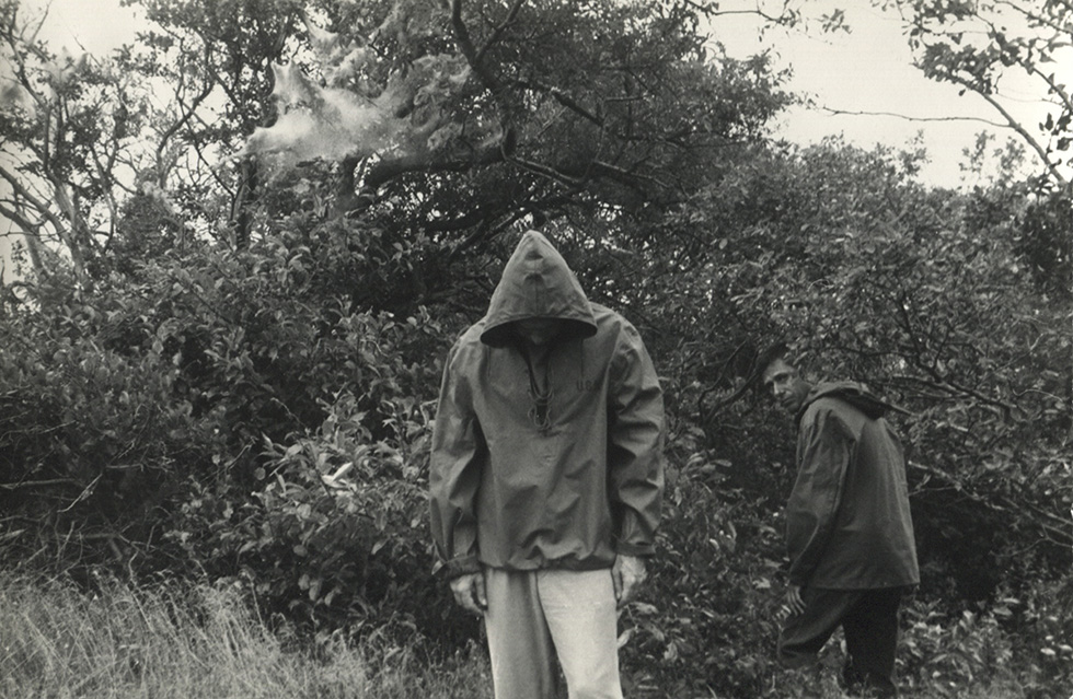 This is a black-and-white photograph of two men wearing hooded rain jackets in a landscape.