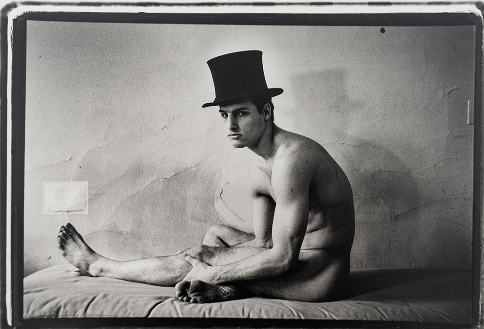 This is a black-and-white photograph of a naked man in profile wearing a top hat.