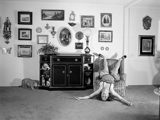 A black and white self portrait photo by Meryl Meisler of the artist upside down in an easy chair in a suburban living room in 1975.