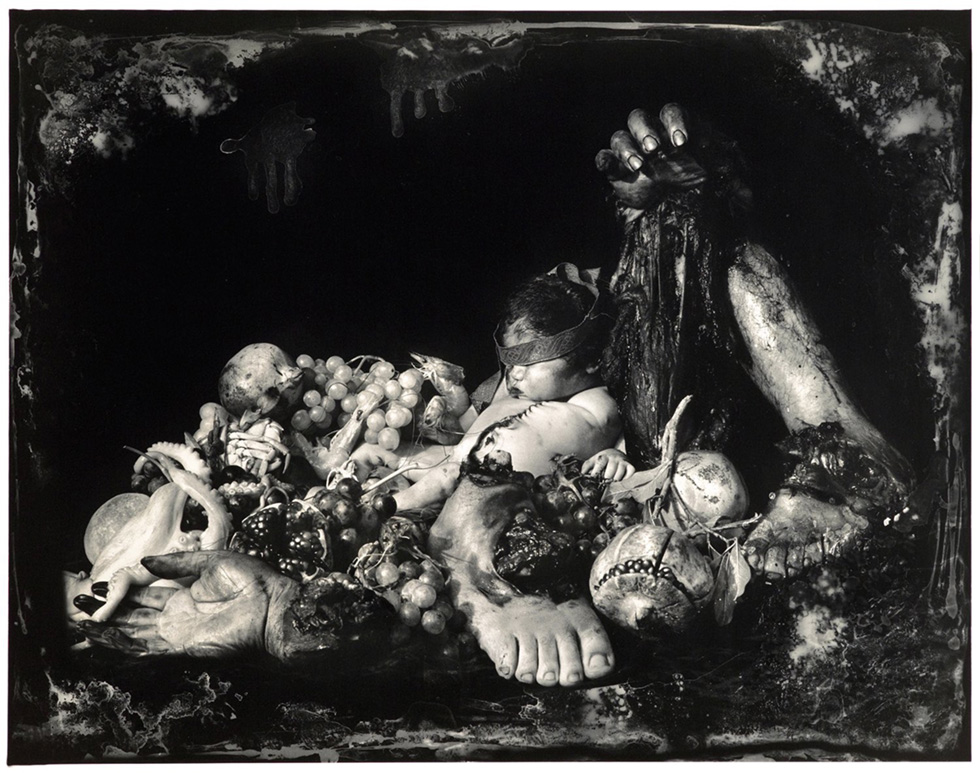 This is an elaborate black and white photographic still life by Joel-Peter Witkin titled "Feast of Fools" picturing human limbs, a baby corpse, an octopus, and fruit.