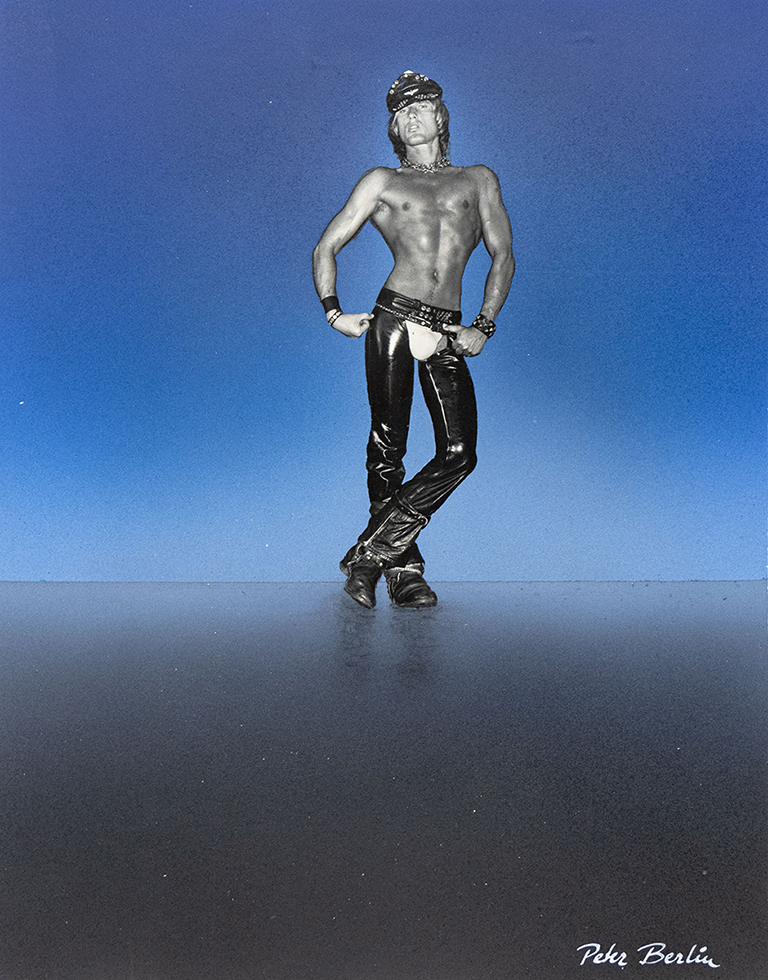 This is a self portrait photograph by Peter Berlin wearing shiny, black trousers in front of a glowing blue background