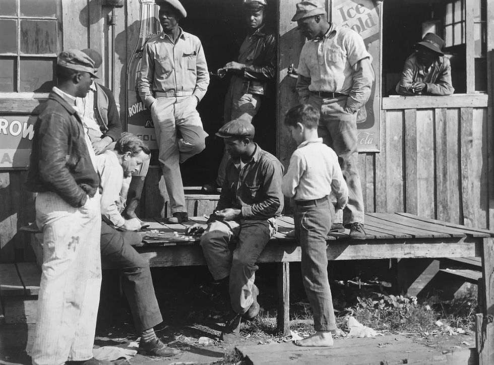 This is a black-and-white photograph of migrant pickers playing checkers on a wood porch in 1939.