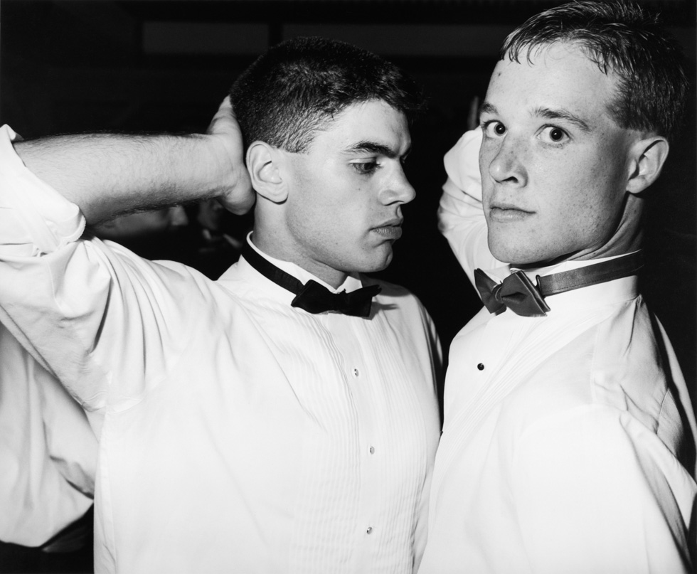 This is a black and white photograph of two young men in tuxedo shirts and bowties at a prom.