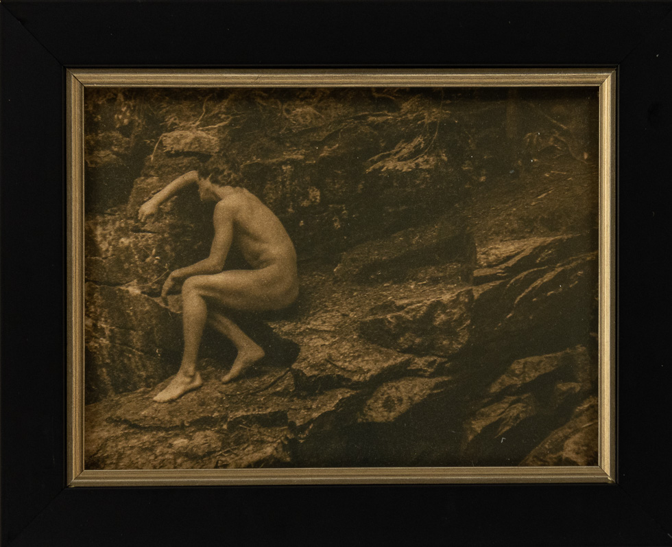 A toned cyanotype photograph by artist Curtice Taylor titled "Orpheus Weeping" which pictures a nude man on a rock.