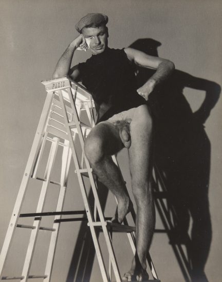 This is a black-and-white photograph of a man standing on a ladder wearing a shirt and checkered hat and no trousers.