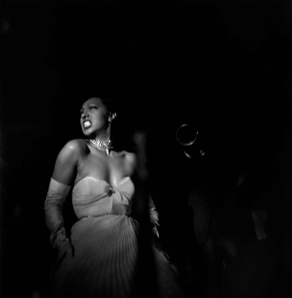 A black-and-white photograph of Josephine Baker in a white dress and long gloves against a black background.