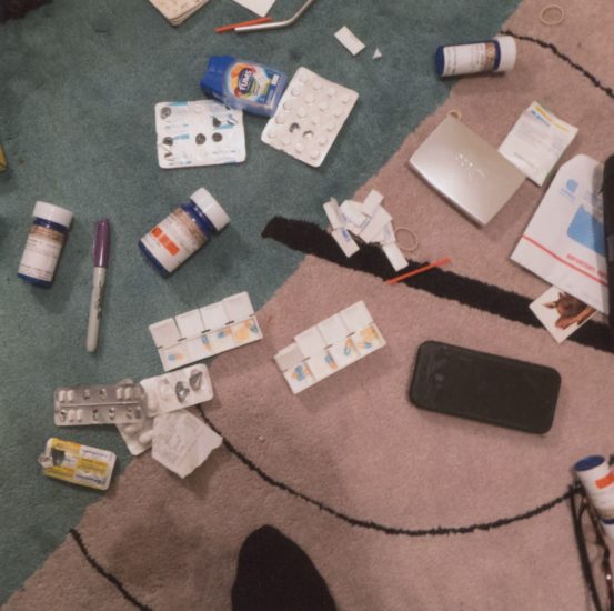 This is a color photograph of different pills strewn on a pink and teal rug shot from above.