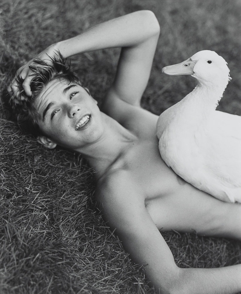 Photograph of a Young man lying in the grass with a duck sitting on his chest