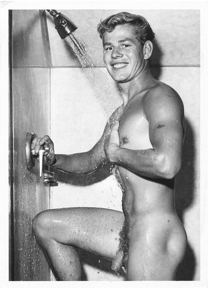 This is a black and white photograph of a smiling young man in the shower.