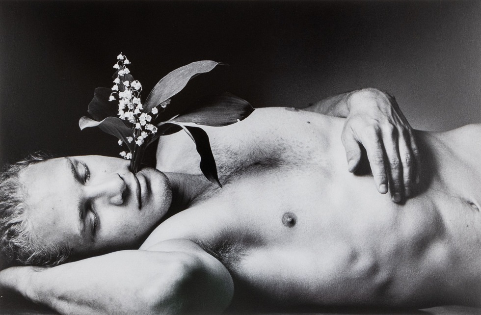 Black and white photograph by Duane Michals of a handsome blond man lying on his back with a flower