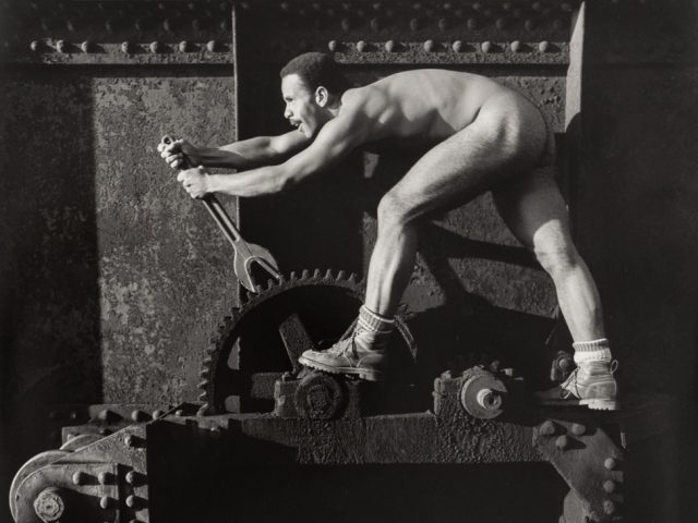 This is a black and white photograph taken by Arthur Tress in the 1970s of a nude man using a wrench on various machinery.