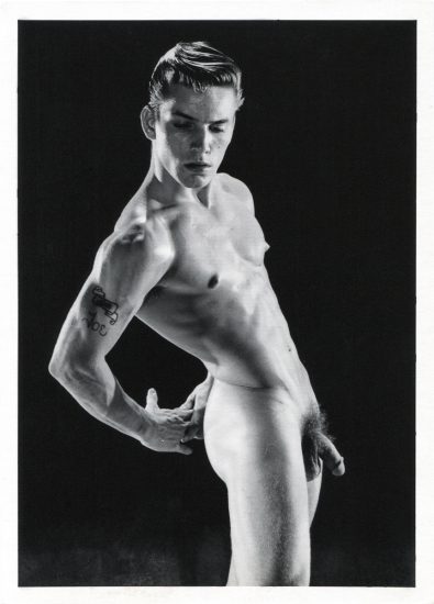 This is a black and white photograph by Bruce of Los Angeles of Joe Dallesandro standing naked posing with his arms behind his back.