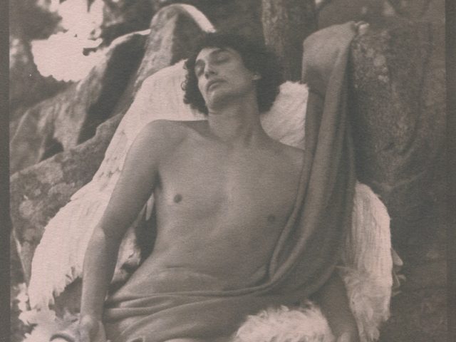 This is a photograph by Curtice Taylor titled "Fallen Angel" of a nude man covered in a cloth with angel wings.