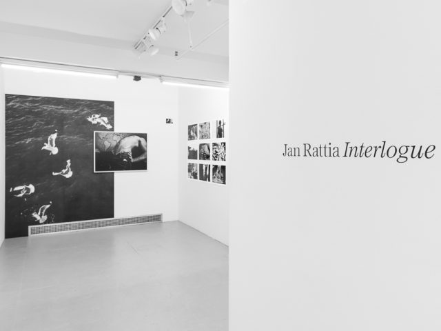 This is a photograph of a white-walled art gallery with black and white photographs on the wall.