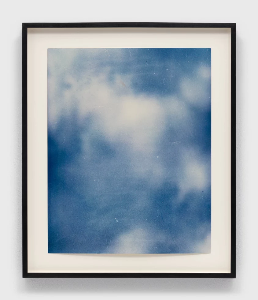 This is a blue and white photograph in a black frame with white border of white clouds in a blue sky.