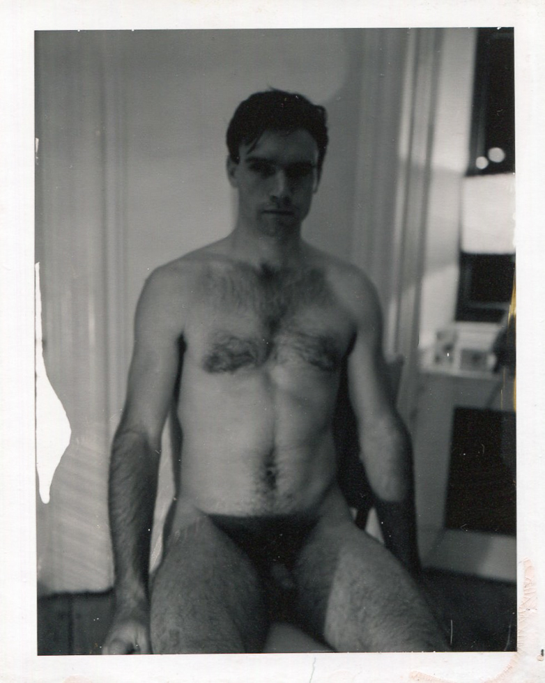 This is a black-and-white nude portrait of a man seated facing the camera directly.