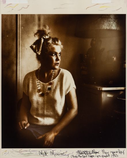 This is a sepia-toned photograph of a woman wearing a bow in her hair looking out a window.