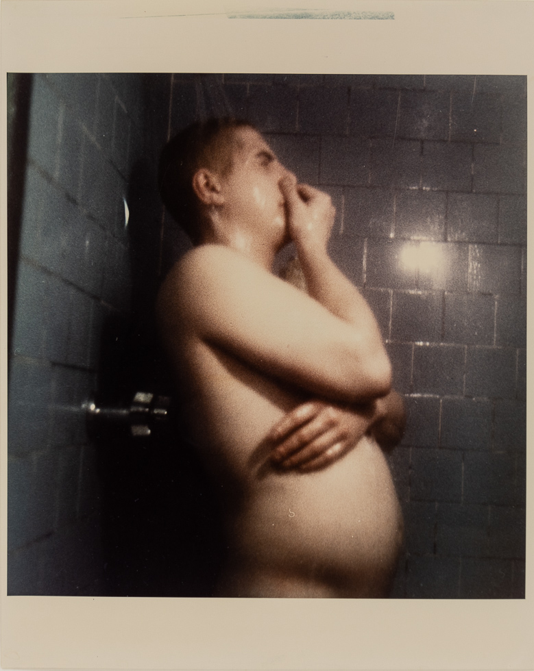 This is a photograph of a man in a shower holding his nose.