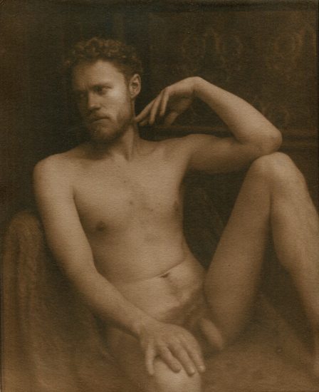 This is a sepia tone photograph of a nude man sitting with his leg raised.