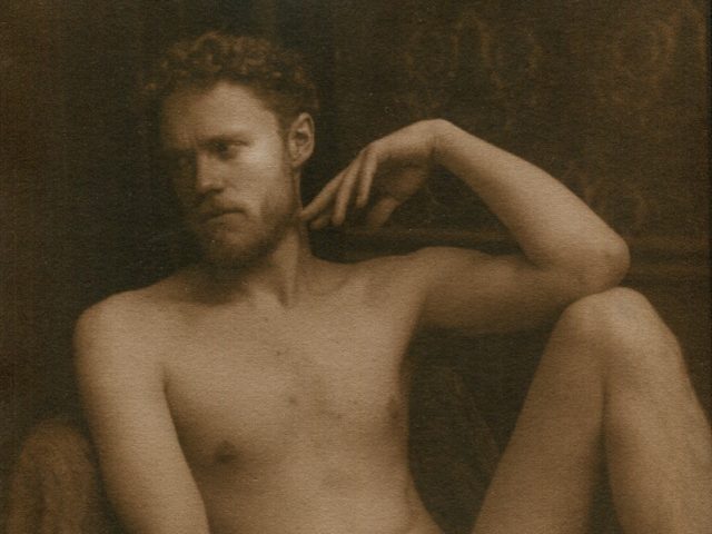 This is a sepia tone photograph of a nude man sitting with his leg raised.