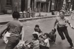 This is a black and white photograph of a police woman playing with children in the street in Harlem in the 1970s.