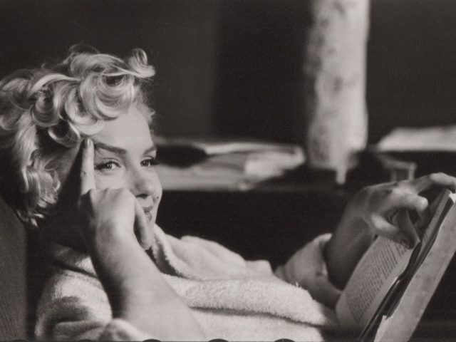This is a black and white photograph of Marilyn Monroe sitting with her right hand on her face.