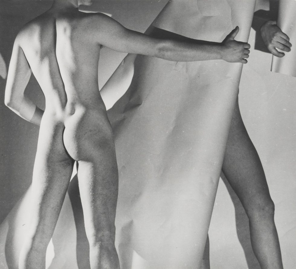 This is a black-and-white photograph of two nude men with a paper backdrop and studio lighting.