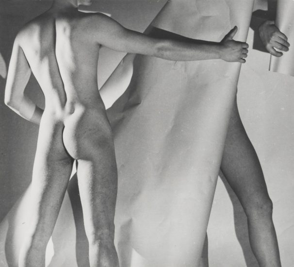 This is a black-and-white photograph of two nude men with a paper backdrop and studio lighting.