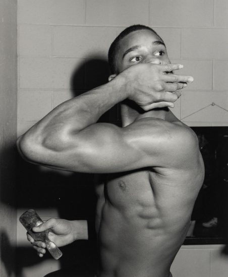 This is a black and white photograph of a shirtless man looking over his shoulder.