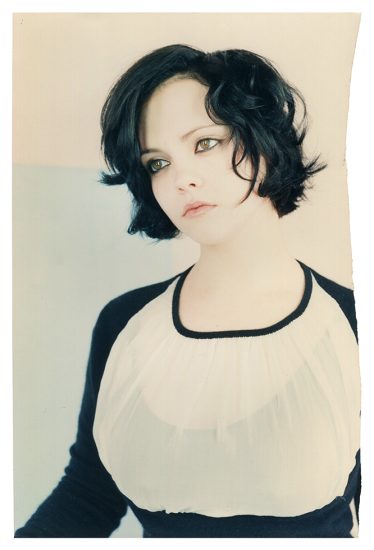 This is a photograph of a woman with short dark hair and hazel eyes in a black and white top against a white background.