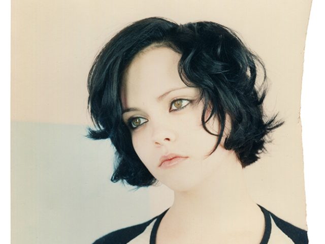 This is a photograph of a woman with short dark hair and hazel eyes in a black and white top against a white background.