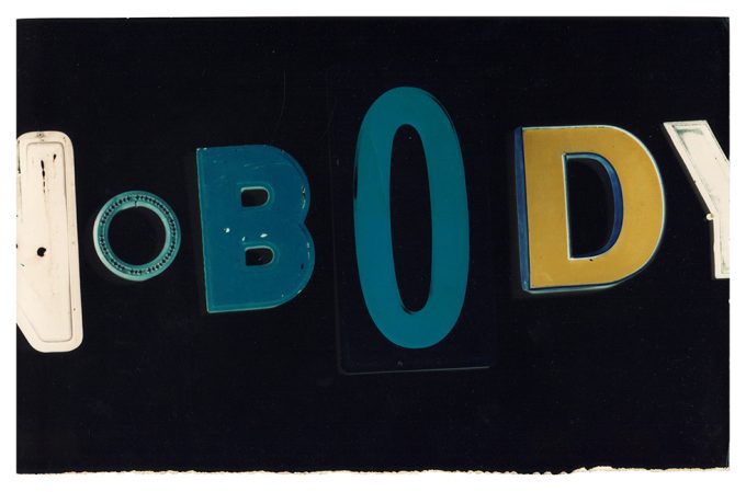 This is a color photograph of blue, yellow, and white letters on a black background spelling the word "nobody."