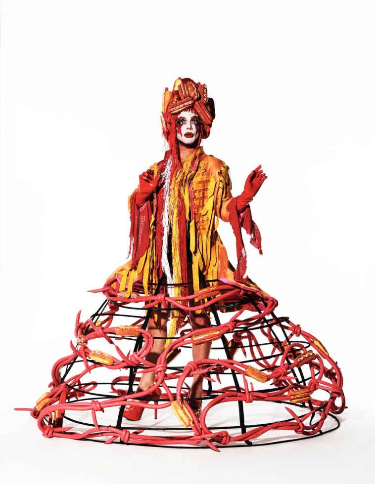 Click to go back. This is a photograph of a person wearing an elaborate costume in front of a white paper backdrop.