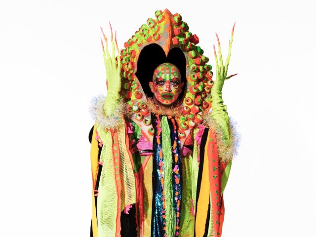 Click for sizes / editions / prices. This is a photograph of a person in an elaborate costume in front of a white background.