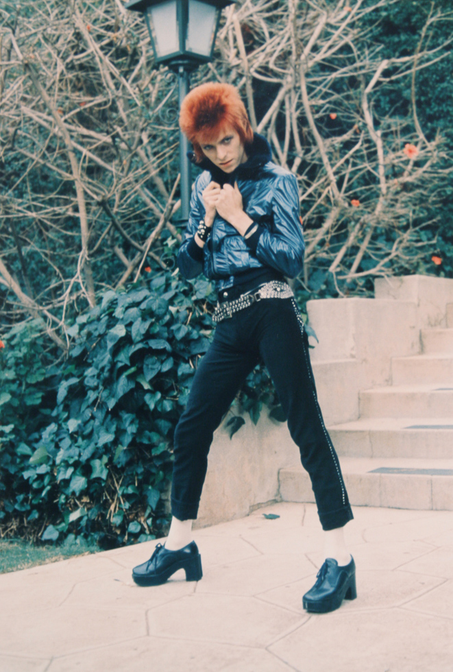 This is a photograph of a man with orange hair wearing black pants and leather shoes.