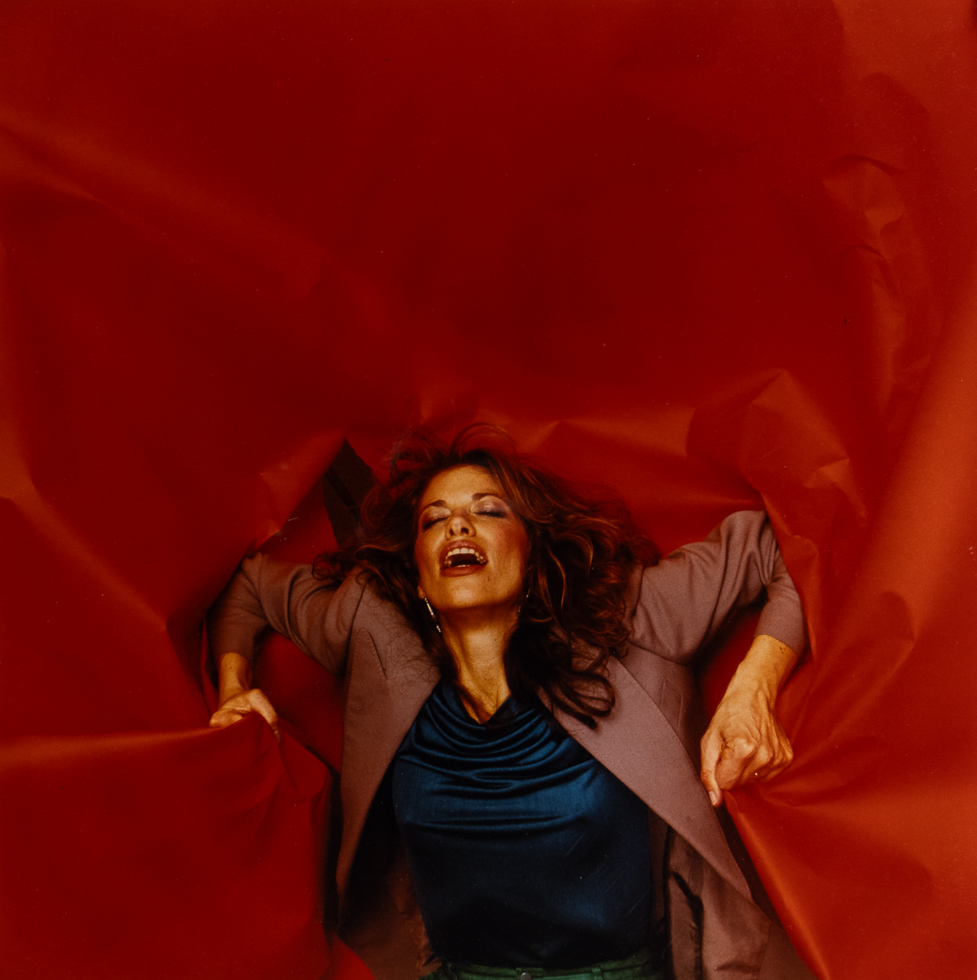 This is a photograph of Carly Simon against a red backdrop.