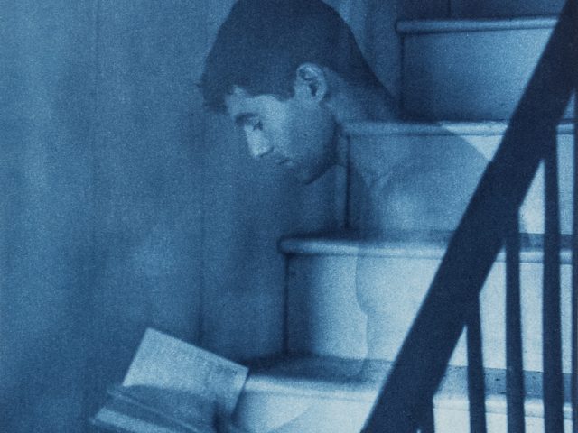 This is a blue-toned print of a man reading a book on the stairs in the nude.