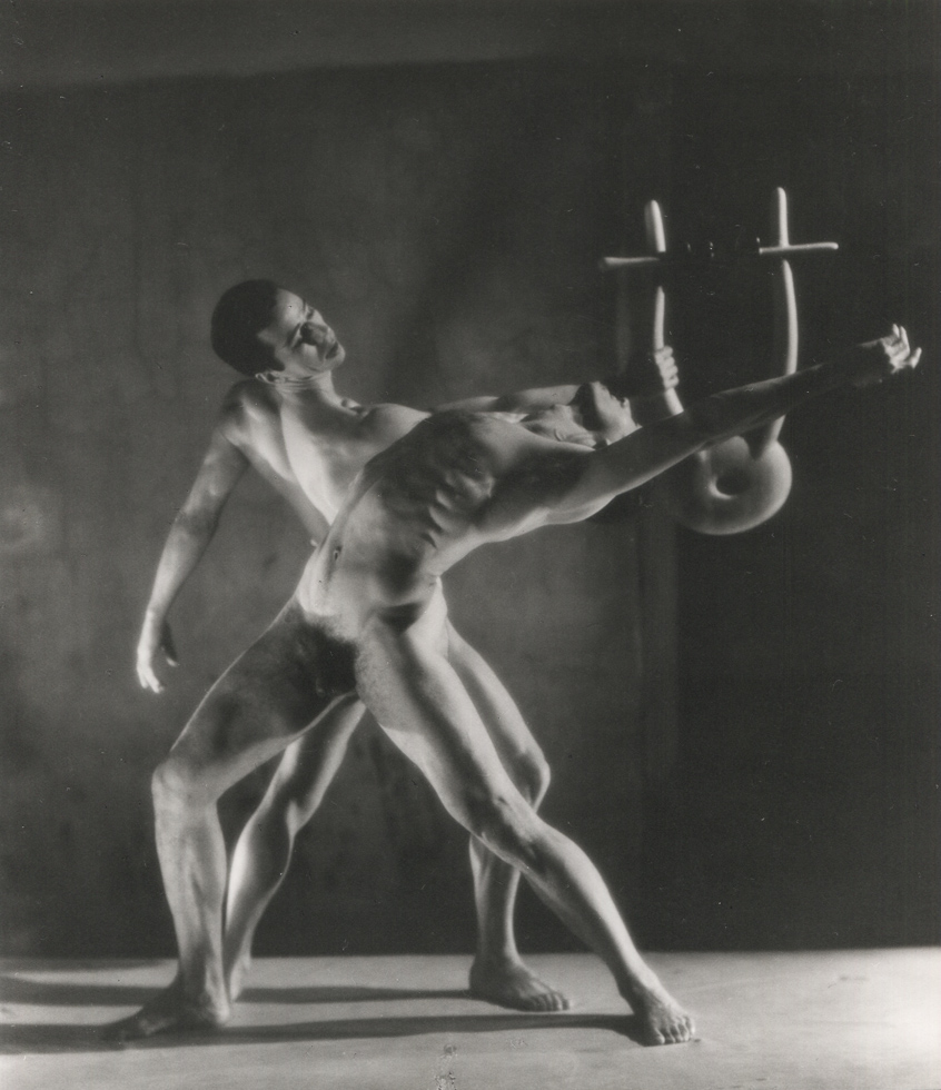 This is a black-and-white photograph of two nude dancers in front of a dark backdrop.