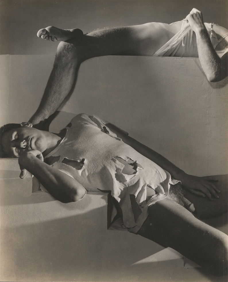 This is a black-and-white photograph of two men (both nude from the waist down) on a photography studio set.