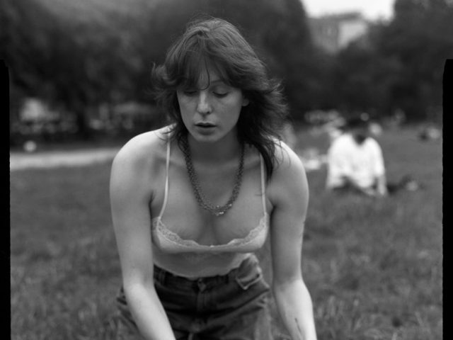 This is a black and white photograph of a woman in a park setting down a record onto a record player.