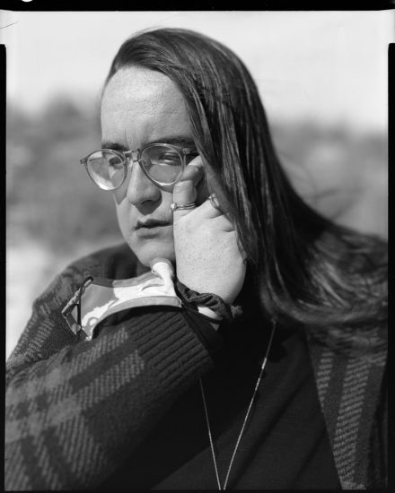 This is a black and white photograph of of a person wiping away a tear from their face while wearing a face mask on their wrist.