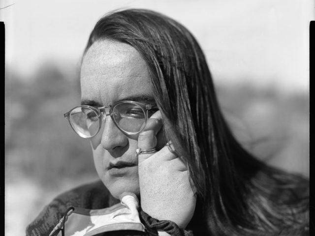 This is a black and white photograph of of a person wiping away a tear from their face while wearing a face mask on their wrist.